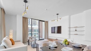 Een moderne hotelkamer met een zithoek, een bank, een aan de muur bevestigde televisie en een groot raam met gordijnen.