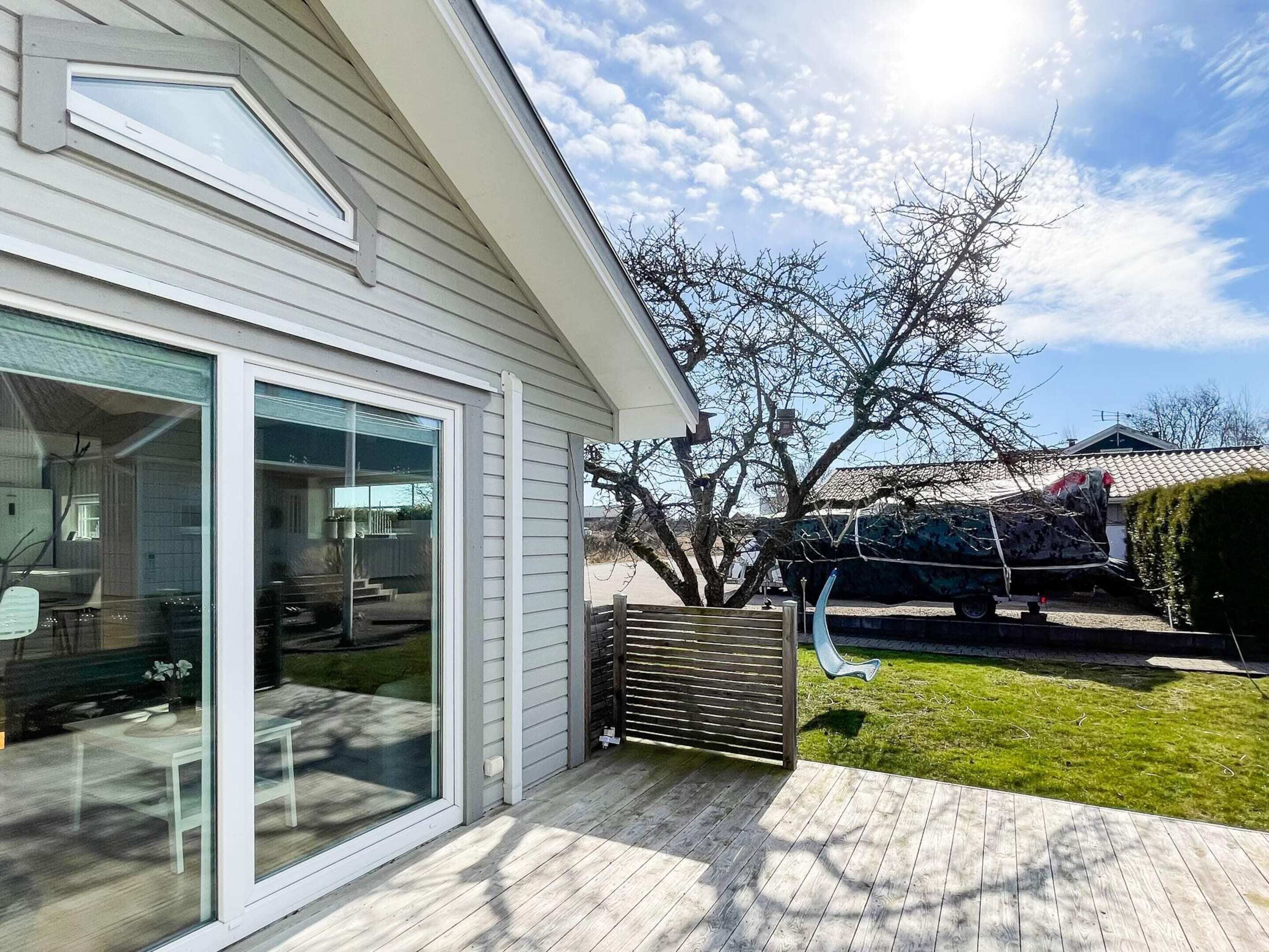 A modern house with large glass doors, a wooden deck, and a tree in the yard.