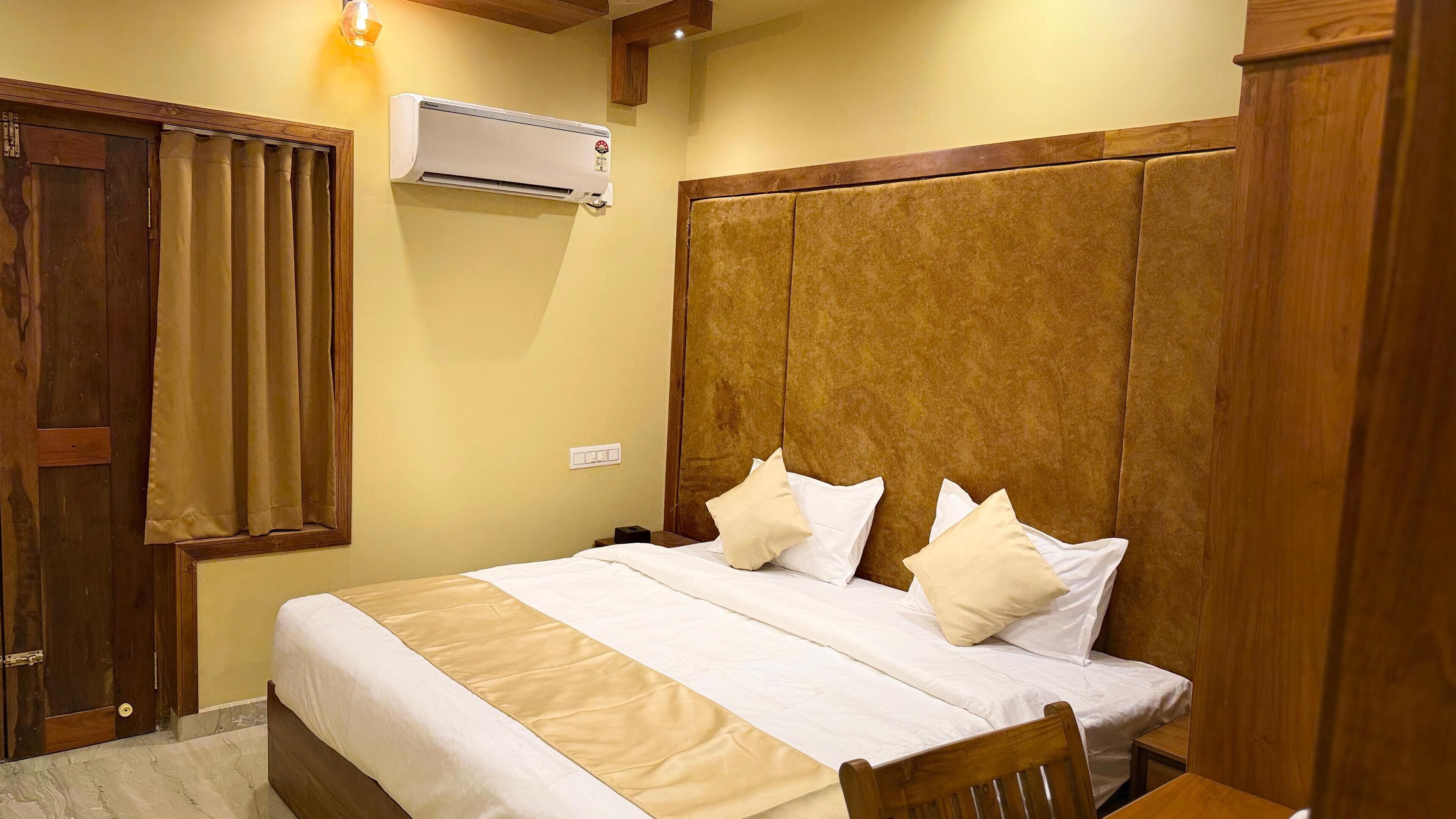 A hotel room with a large bed, wooden headboard, and an air conditioning unit on the wall.