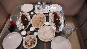 A table set with various dishes including foil-wrapped food, rice, and flatbreads, along with condiments and glasses.