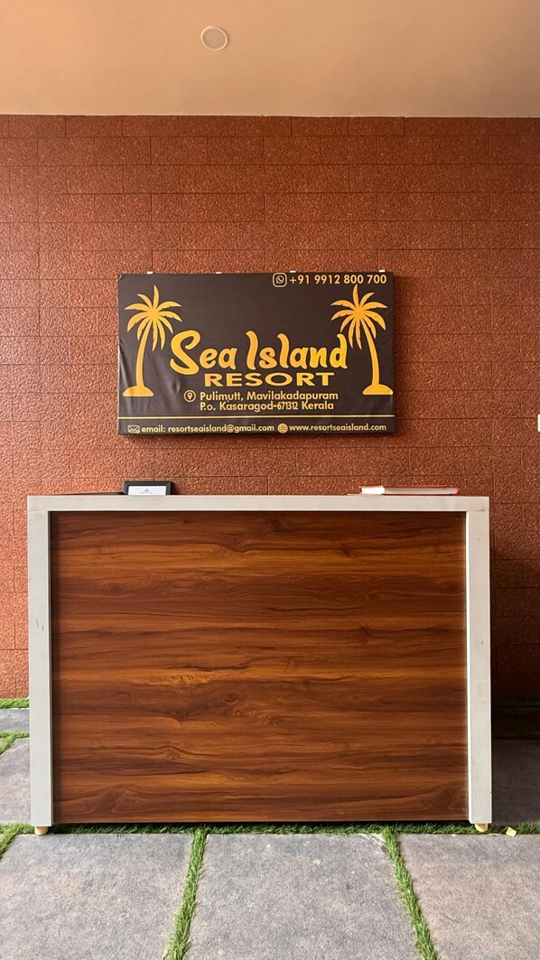 A reception desk with a sign for Sea Island Resort, including contact information and location details. - Sea Island Resort (Hosdurg)