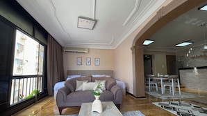 Una habitación de hotel moderna con un ventanal grande, un sofá, una mesa de centro y un área de comedor con sillas y una mesa.