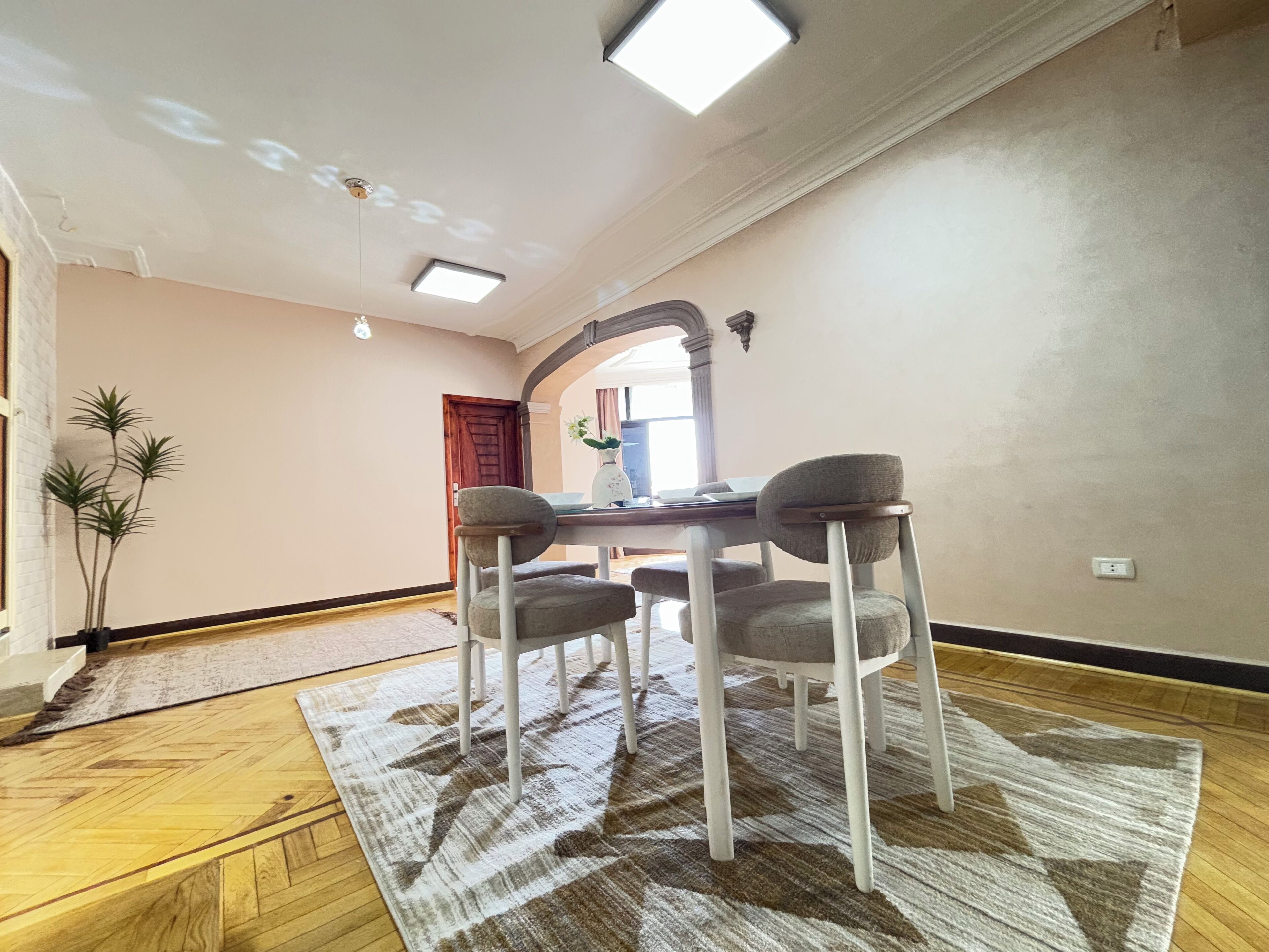 A dining area with a table and four chairs, a patterned rug, and a wooden floor.