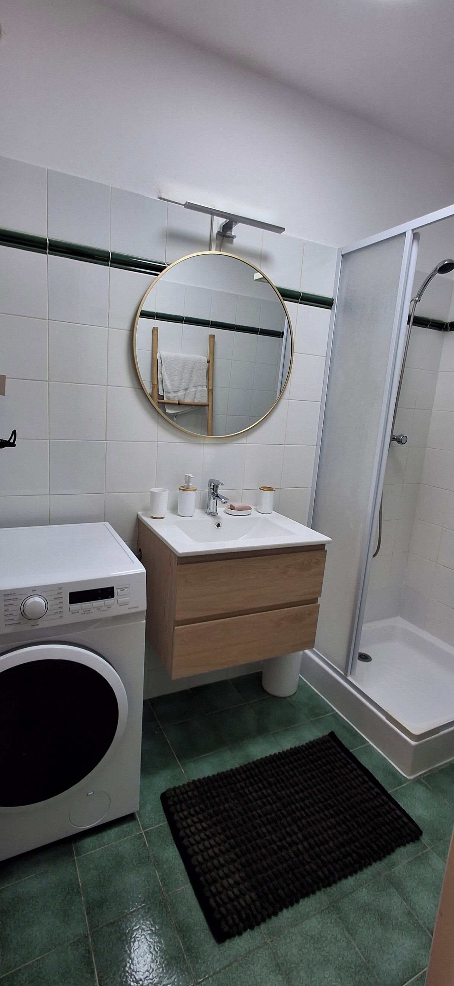 A bathroom with a washing machine, a sink with a mirror, and a shower.