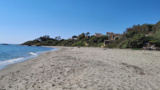 Una playa arenosa con cielo azul despejado, algunos edificios en una colina y el océano al fondo.