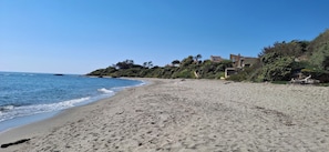 A sandy beach with a clear blue sky, a few buildings on a hillside, and the ocean in the background. - Apartment in a residential complex with two pools, 100 meters from the beach (Linguizzetta)
