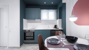 A modern kitchen with teal cabinets, a white countertop, and a dining area with a table set for two. - Beachfront Oasis by Luxlikehome (Psakoudia Halkidiki)