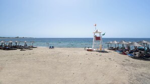 A beach with a lifeguard tower, umbrellas, and lounge chairs. - Beachfront Oasis by Luxlikehome (Psakoudia Halkidiki)