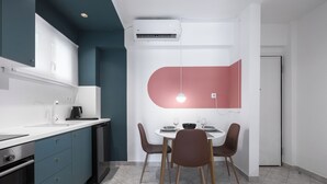 A modern kitchen with teal cabinets, a white countertop, and a dining area with a red accent wall and two brown chairs. - Beachfront Oasis by Luxlikehome (Psakoudia Halkidiki)