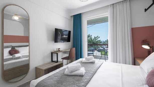 A modern hotel room with a large bed, a desk, a chair, a TV, and a balcony with a view. - Beachfront Oasis by Luxlikehome (Psakoudia Halkidiki)