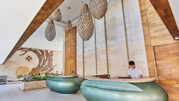 A reception area with a receptionist, large green planters, wooden accents, and a mural on the wall.