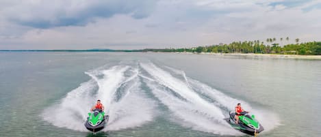 Two jet skis on a calm body of water with a beach and palm trees in the background.
