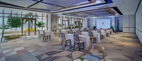 Una amplia sala de conferencias con varias mesas y sillas, ventanas grandes que ofrecen vistas al exterior y un diseño de techo moderno.
