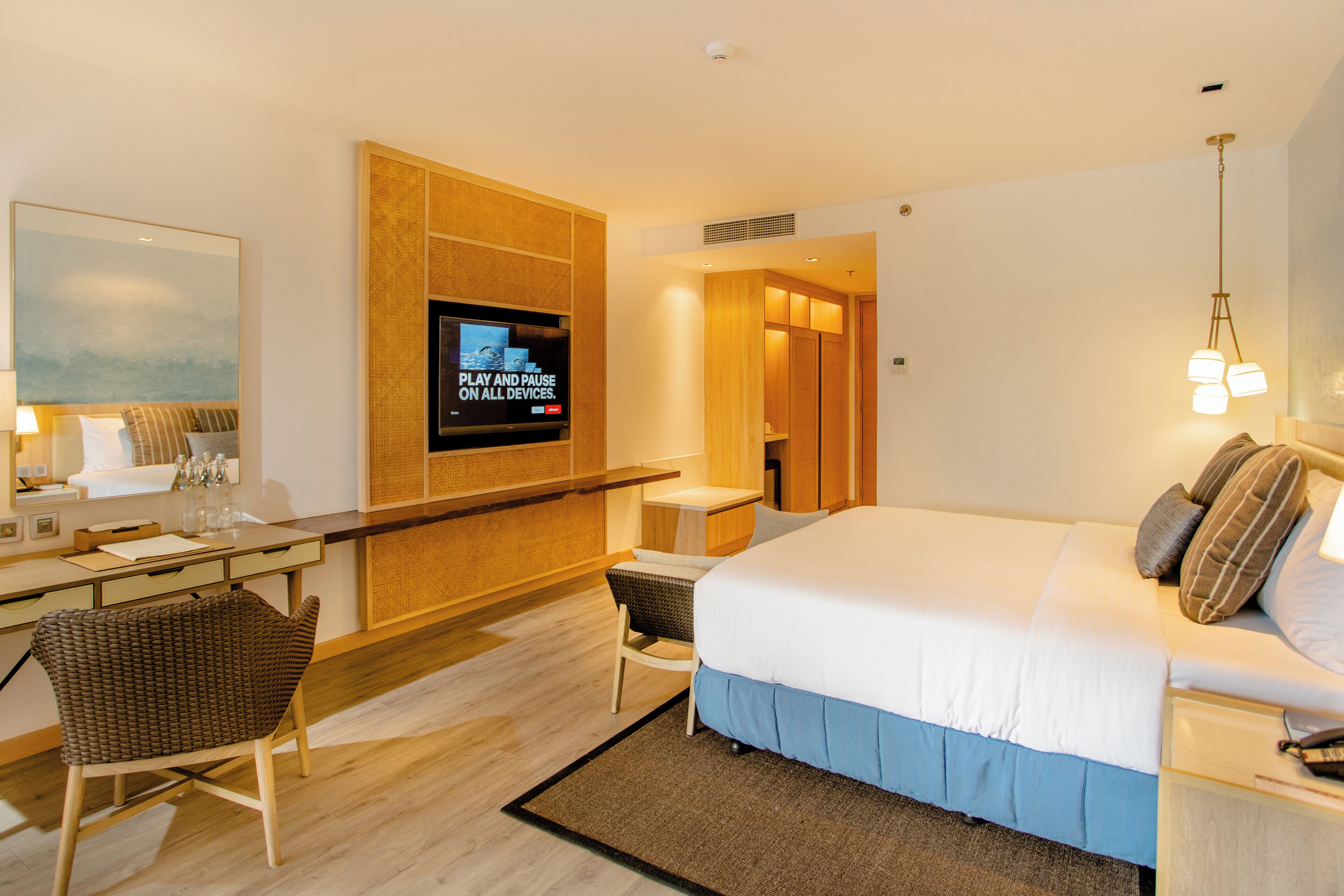 A modern hotel room with a large bed, a desk with a chair, a television, and a view of the city.