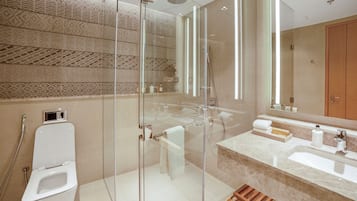 A modern bathroom with a glass-enclosed shower, a white toilet, a sink with a marble countertop, and a wooden basket.