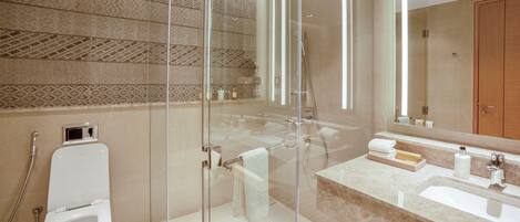 Un baño moderno con ducha de vidrio, inodoro blanco, lavamanos con encimera de mármol y una cesta de madera.