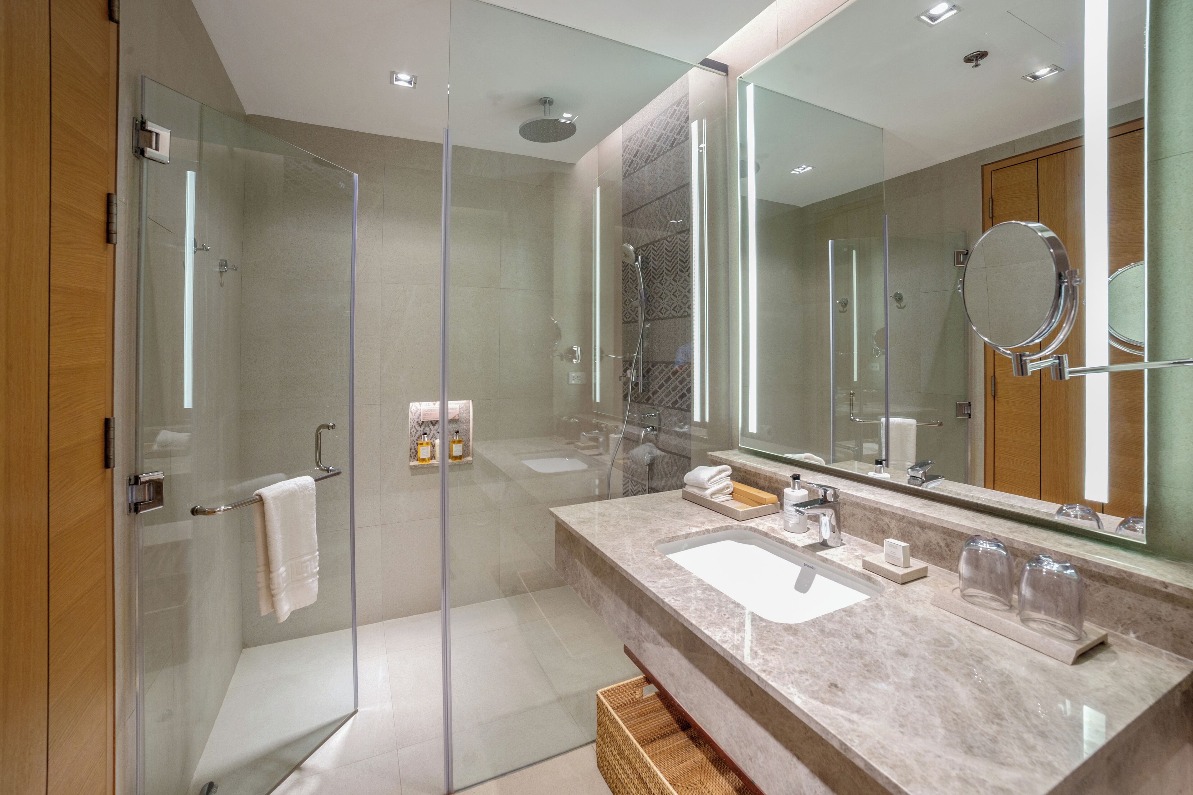 A modern bathroom with a glass-enclosed shower, a large mirror, and a marble countertop with a sink and vanity.