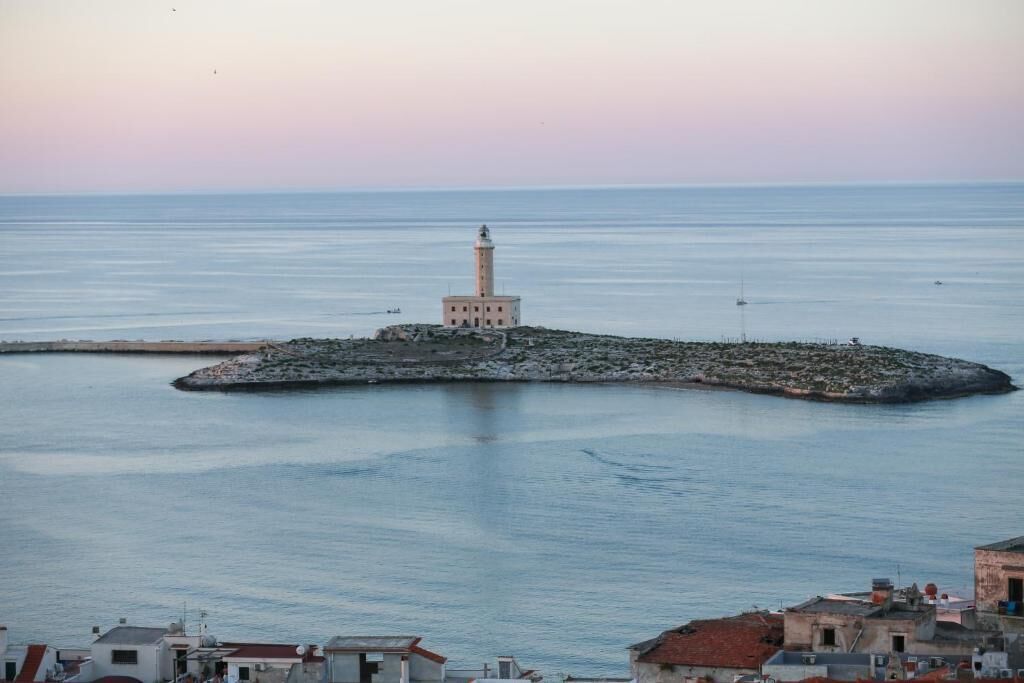 A coastal scene with a lighthouse on a small island, surrounded by calm sea and a few boats.