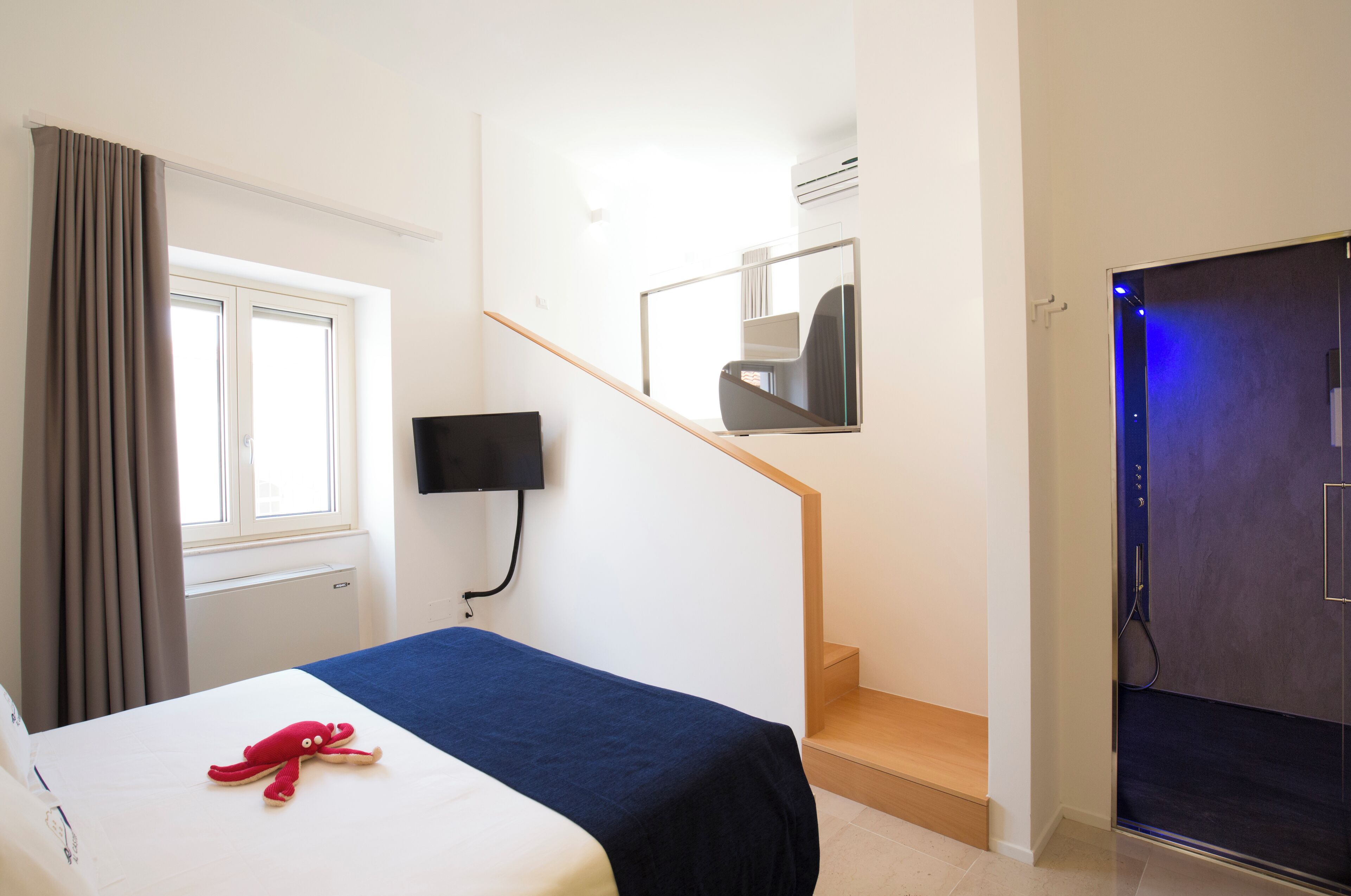 Une chambre d’hôtel avec un lit, une décoration représentant un poulpe rouge, un téléviseur fixé au mur, un escalier et une porte dotée d’un éclairage bleu.