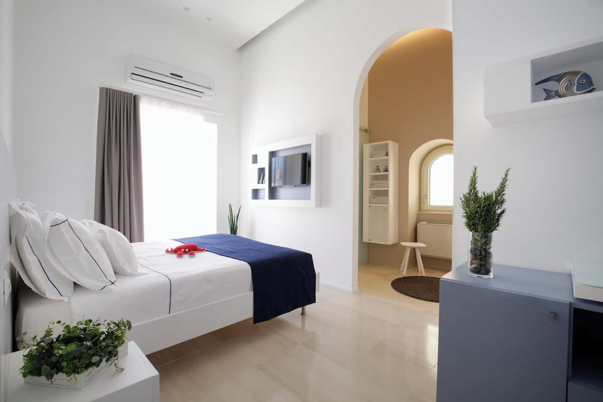 A modern hotel room with a bed, a desk, a TV, and a potted plant.