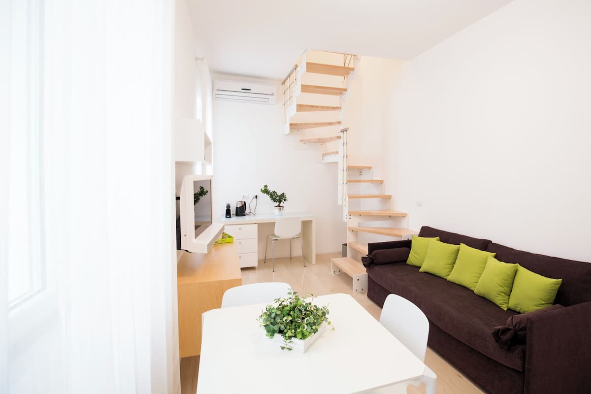 A compact living space with a staircase, a dining area, and a sofa with green cushions.