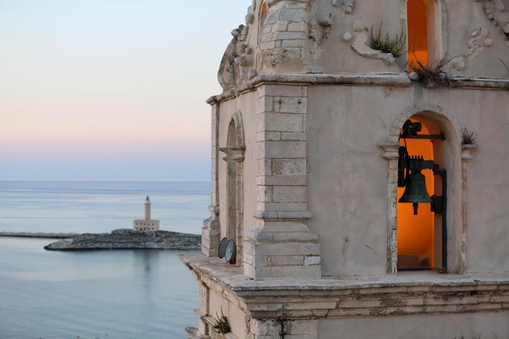 Ein Steingebäude mit einem Glockenturm und einem kleinen Bau auf einem Felsen direkt am Meer.