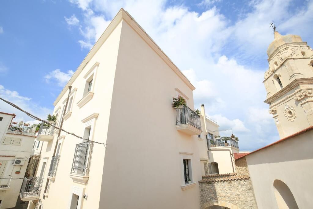 A building with a white facade, a balcony with metal railings, and a bell tower in the background.