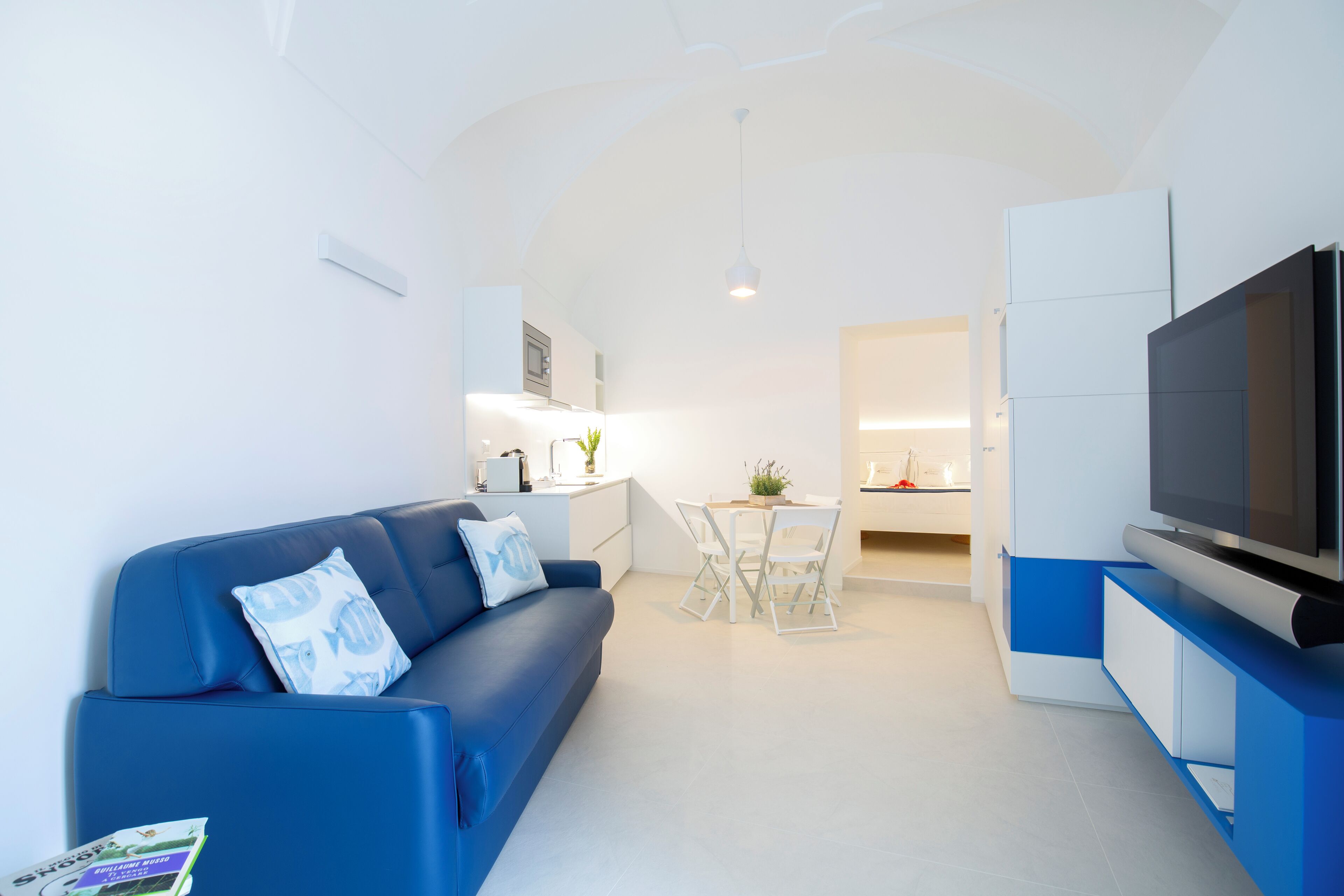 Una sala de estar moderna con un sofá azul, un televisor de pantalla plana y un comedor con mesa y sillas.