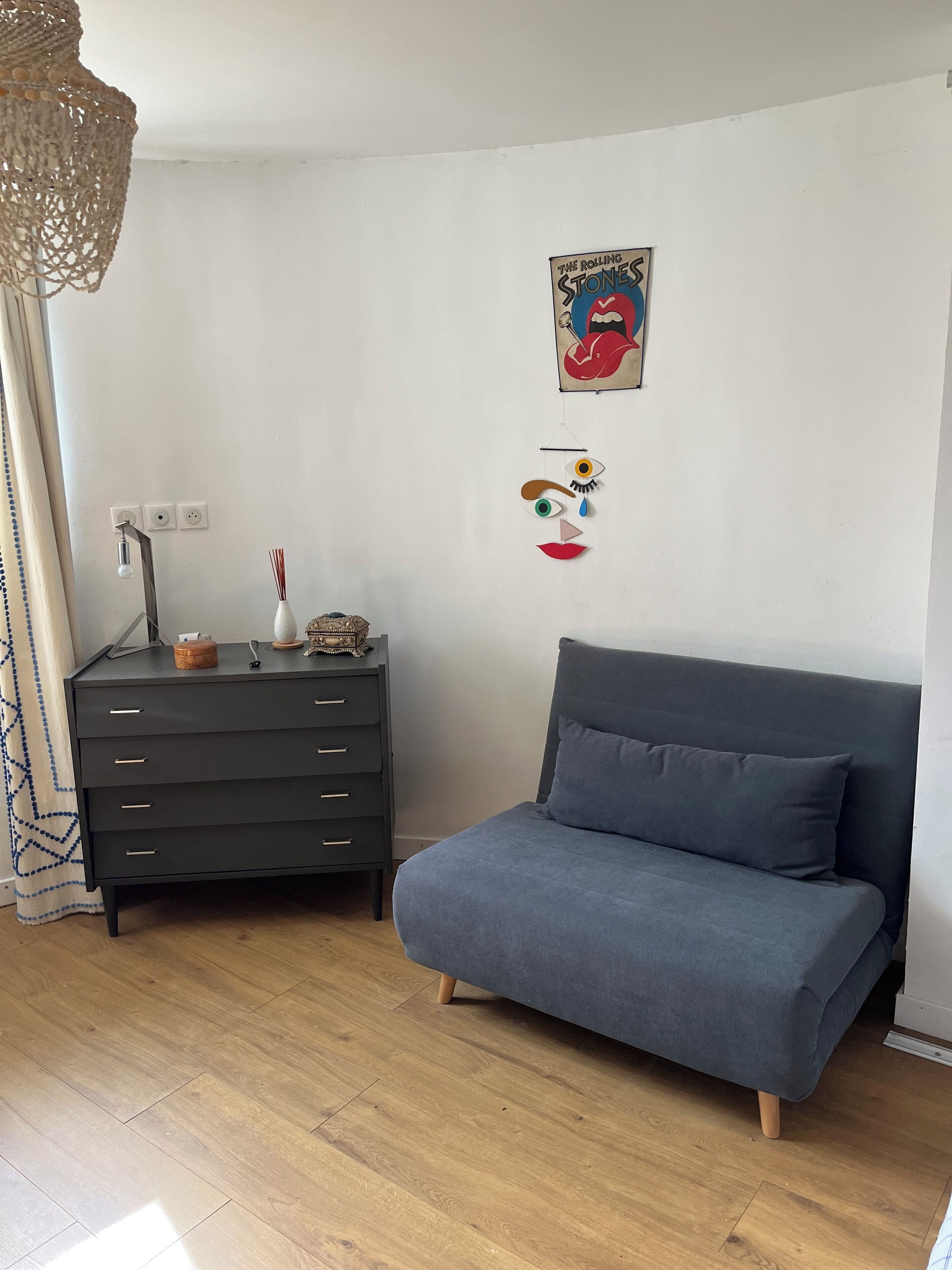 Ein Zimmer mit einer grauen Couch, einem dunklen Holzschrank, einem Wandposter und einer Hängeleuchte.