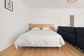 A bedroom with a wooden bed, white bedding, a dark sofa, and a framed picture on the wall. - Superb studio with river access and private square (Vals-les-Bains)