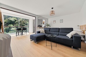A modern living room with a dark grey sectional sofa, a round coffee table, and a dining area with a small table and chairs. - Superb studio with river access and private square (Vals-les-Bains)