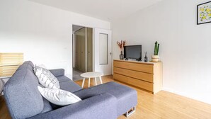 A modern living room with a grey sofa, a small white table, a wooden dresser, and a television. - Superb studio with river access and private square (Vals-les-Bains)