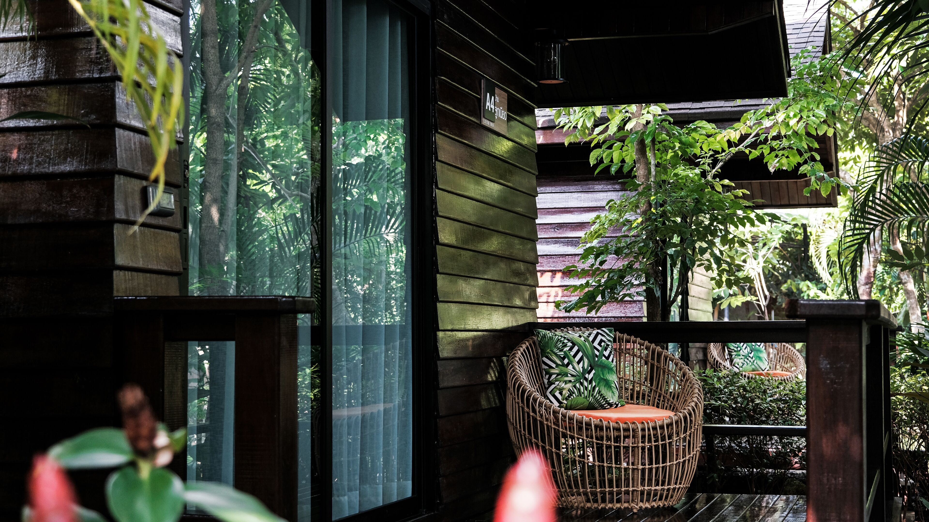 A wooden deck with a wicker chair and a view of a lush garden.