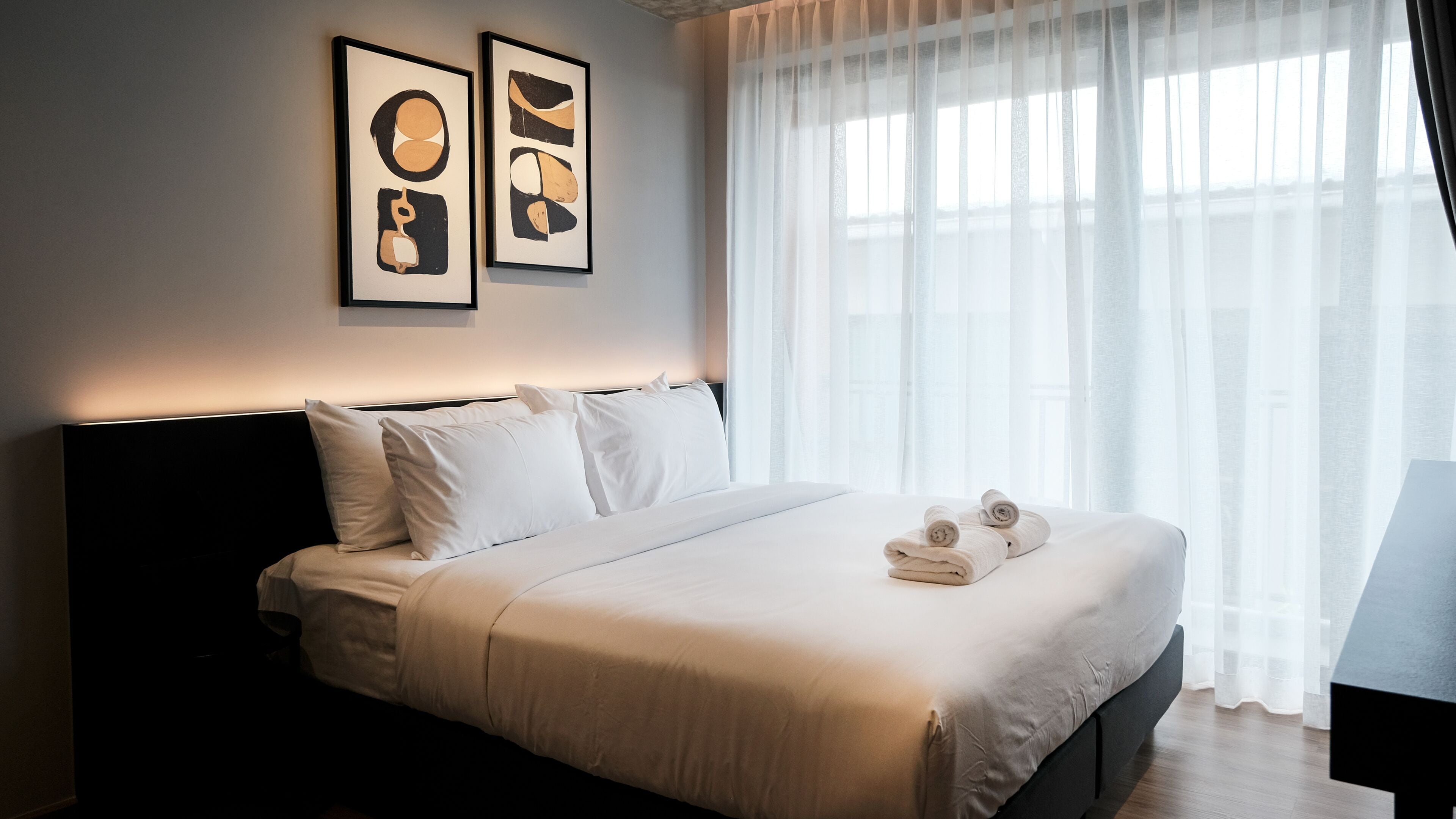A hotel room with a bed, pillows, a bedside table, and two framed artworks on the wall.