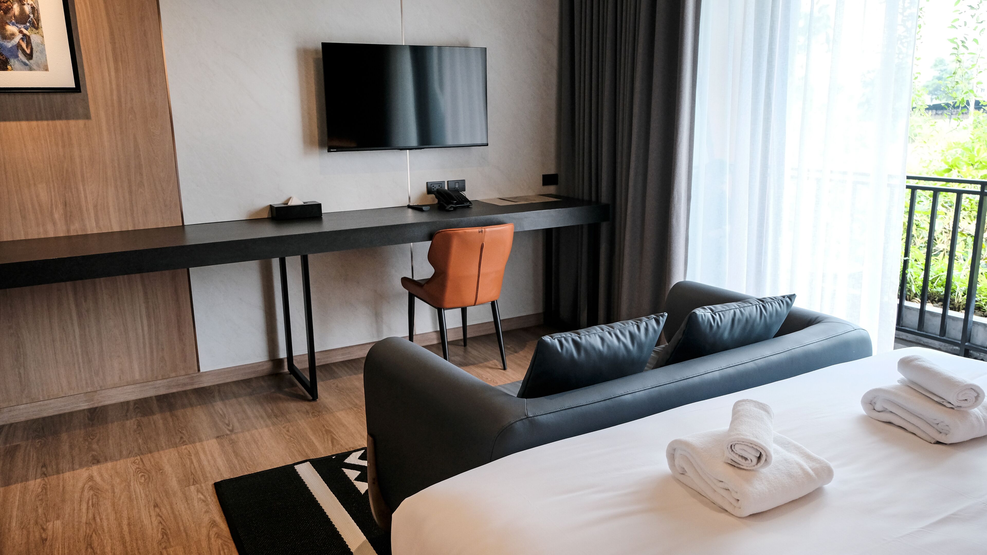 Une chambre d’hôtel moderne équipée d’un lit, d’un bureau, d’une chaise, d’une télévision et offrant une vue sur la verdure environnante.