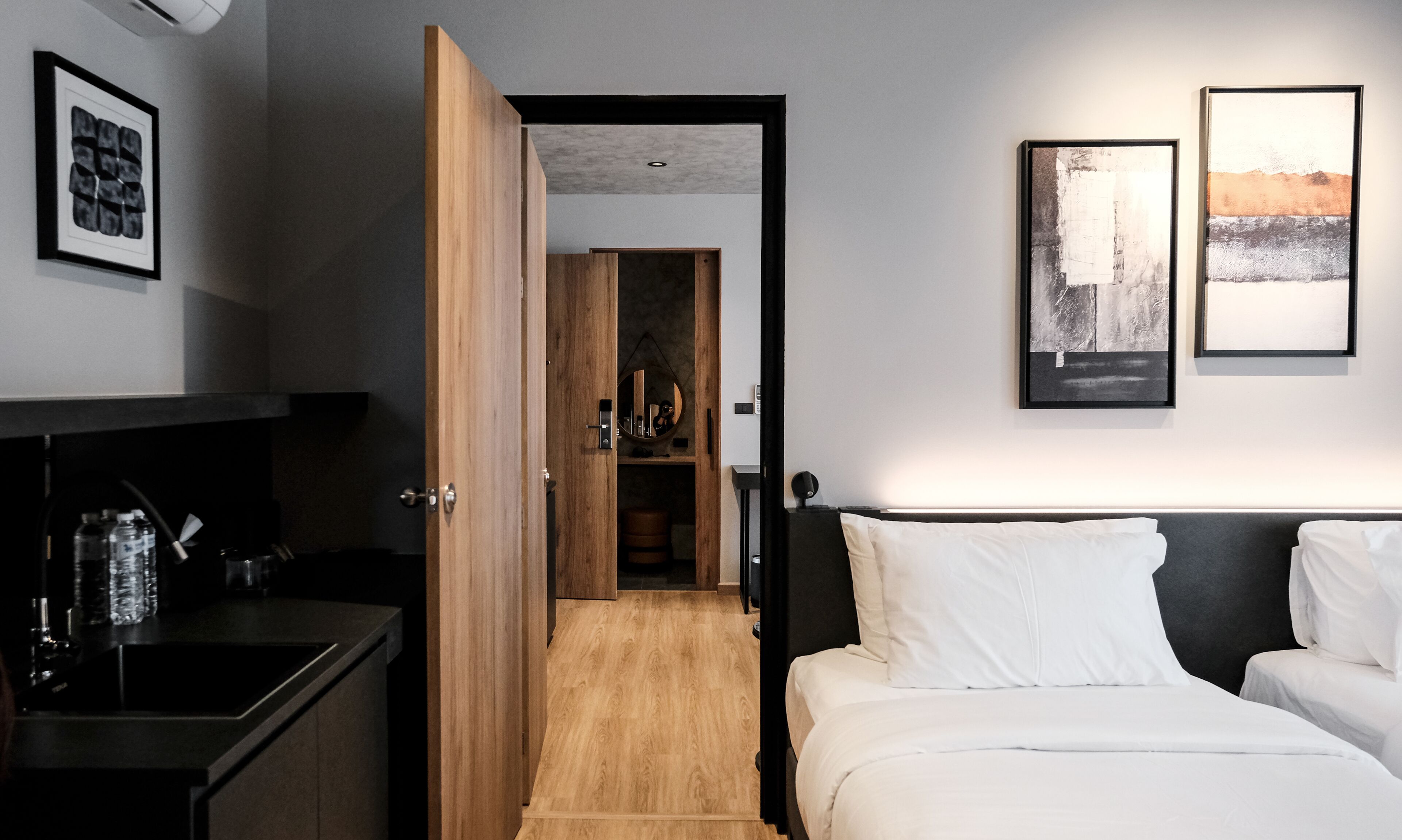 A modern hotel room with a bed, a desk, and a wardrobe. There are two framed artworks on the wall.