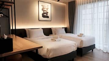 A hotel room with two beds, a bedside table, a wall-mounted artwork, and a window with curtains.