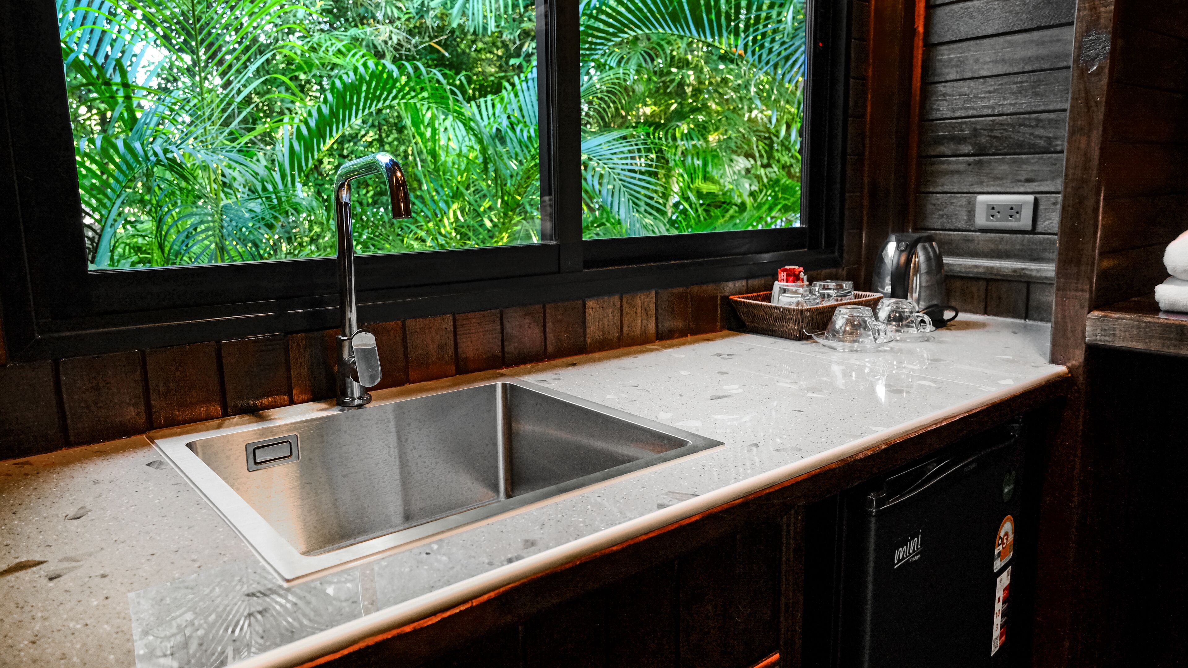A kitchen with a stainless steel sink, a window with a view of greenery, and a coffee maker on the counter.