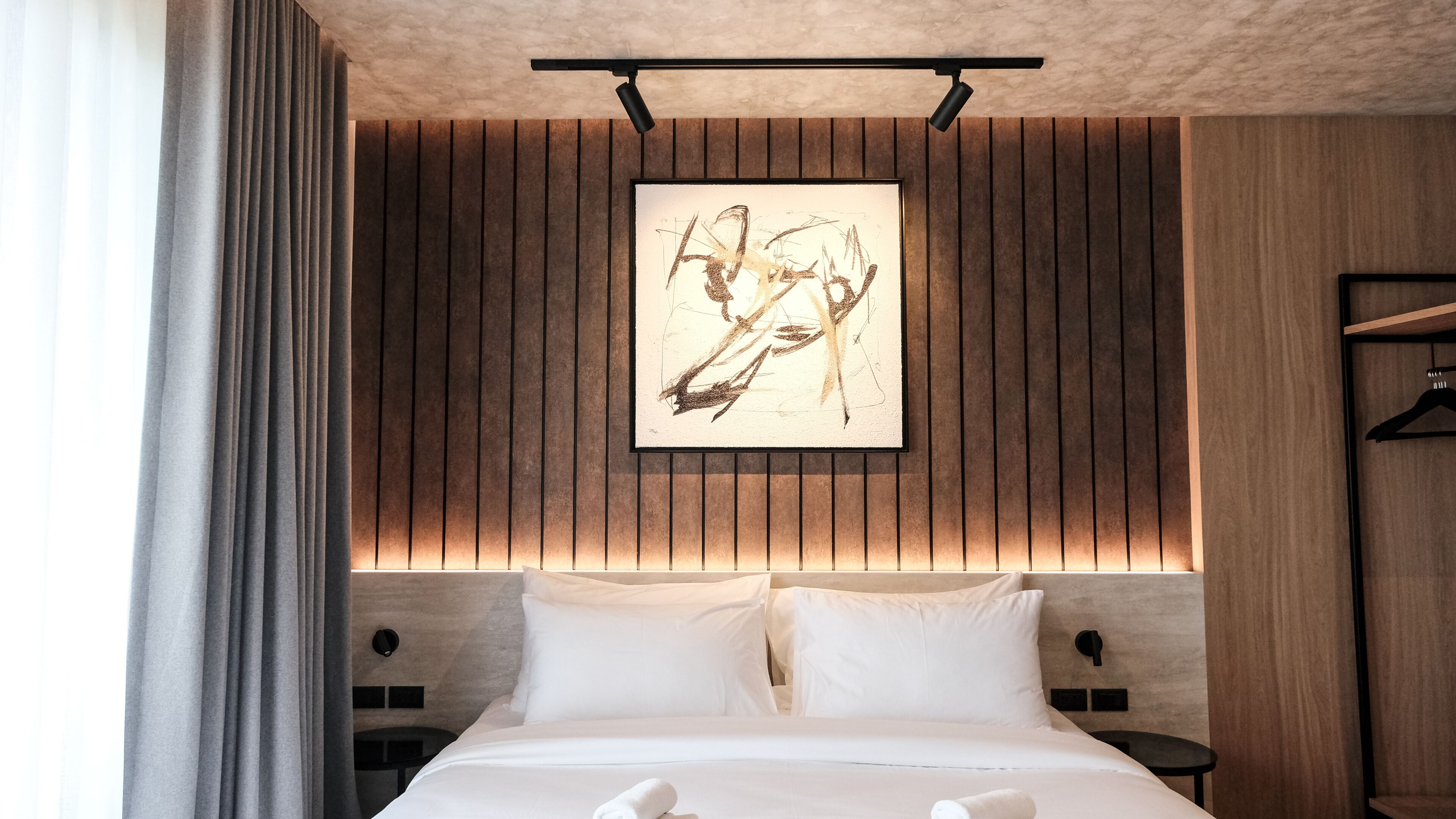 A hotel room with a bed, two bedside tables, a wall-mounted artwork, and a wooden panel design.