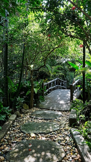 Un sendero de piedra que atraviesa un jardín exuberante con un puente de madera.