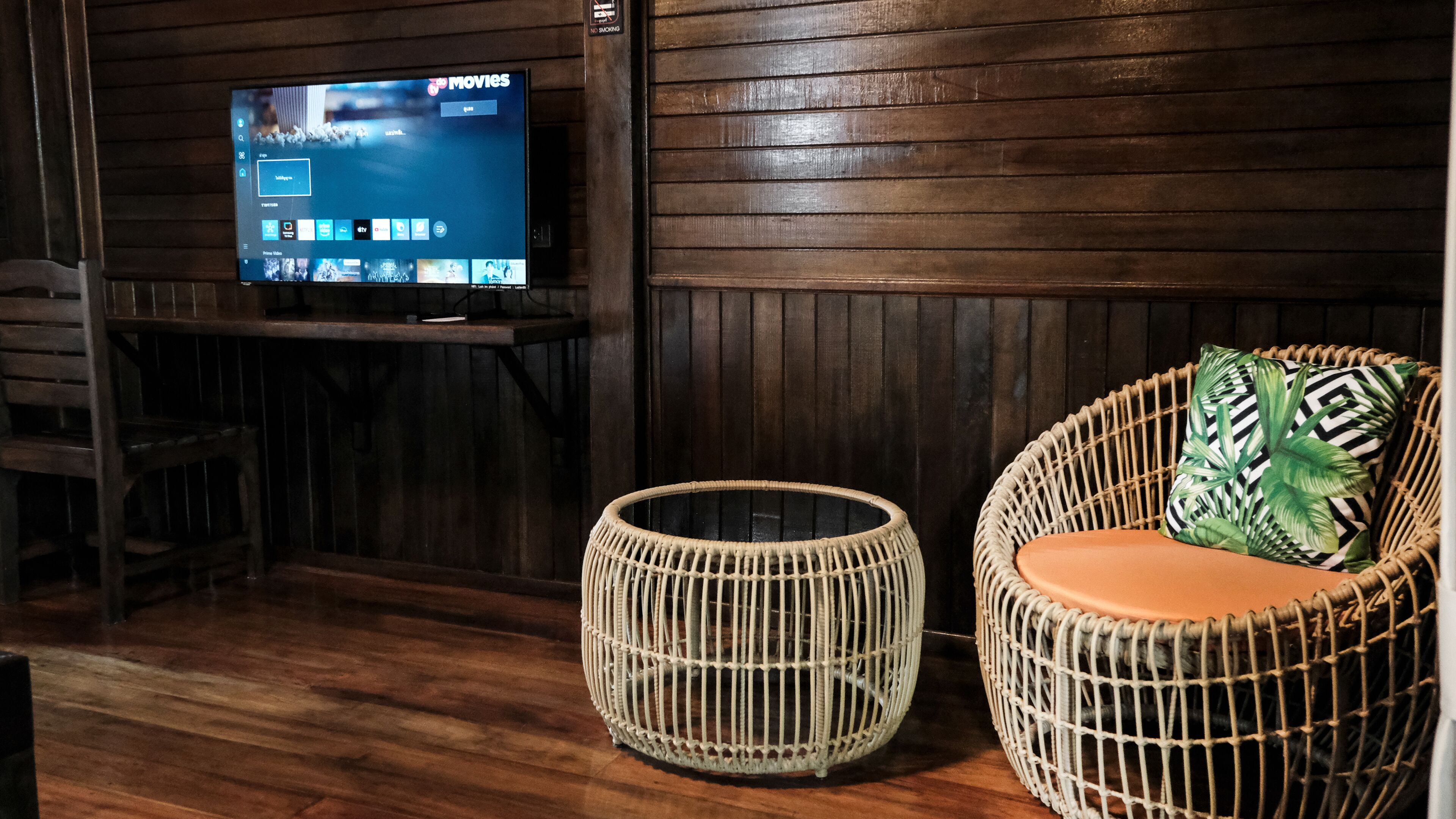 A room with a television on a wooden stand, a wicker chair with a cushion, and a woven stool.