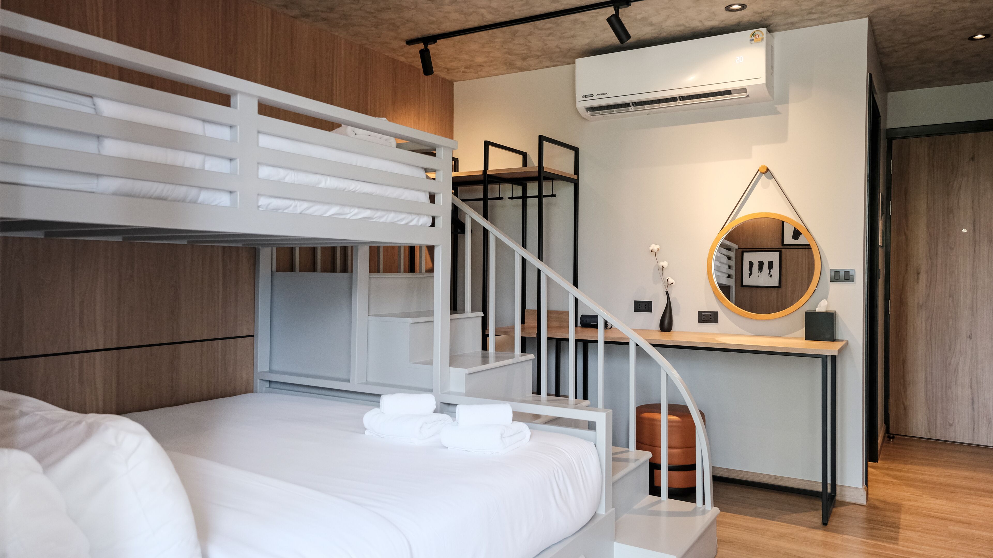 Une chambre moderne avec un lit superposé, un bureau avec une chaise, un appareil de climatisation et un grand miroir rond accroché au mur.