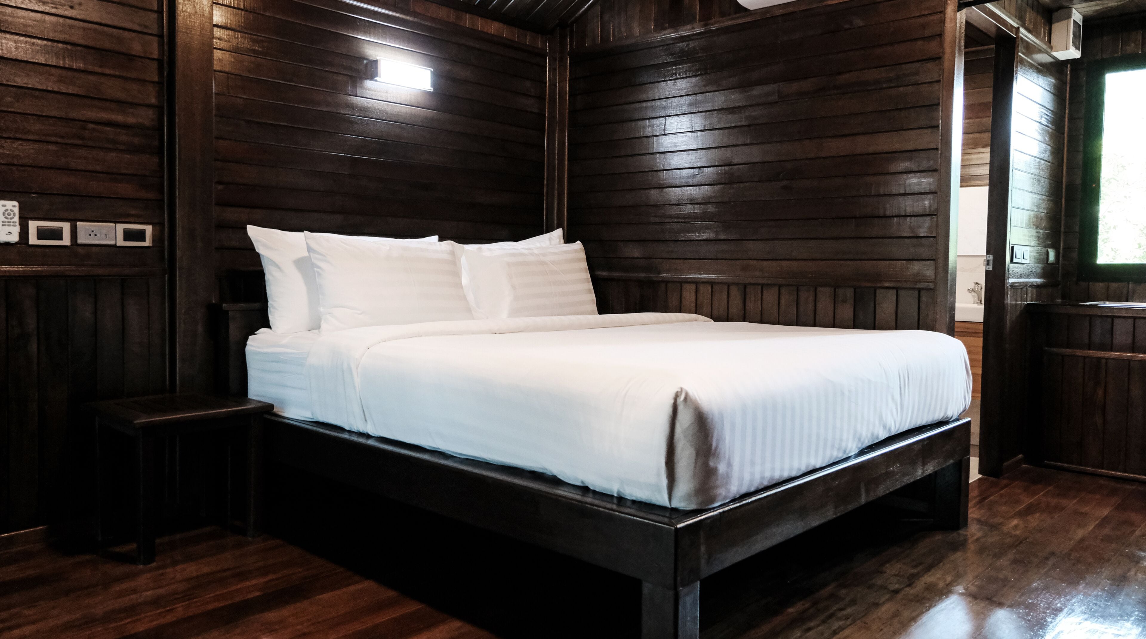 A wooden-framed bed with white bedding in a room with wooden paneling on the walls and a wooden floor.