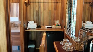 Un baño compacto con paneles de madera, un lavamanos, un refrigerador pequeño y una ventana con persianas.