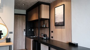 A modern kitchen with wooden cabinetry, a black countertop, and a built-in coffee machine. - Lush Inn Phuket (Chalong)