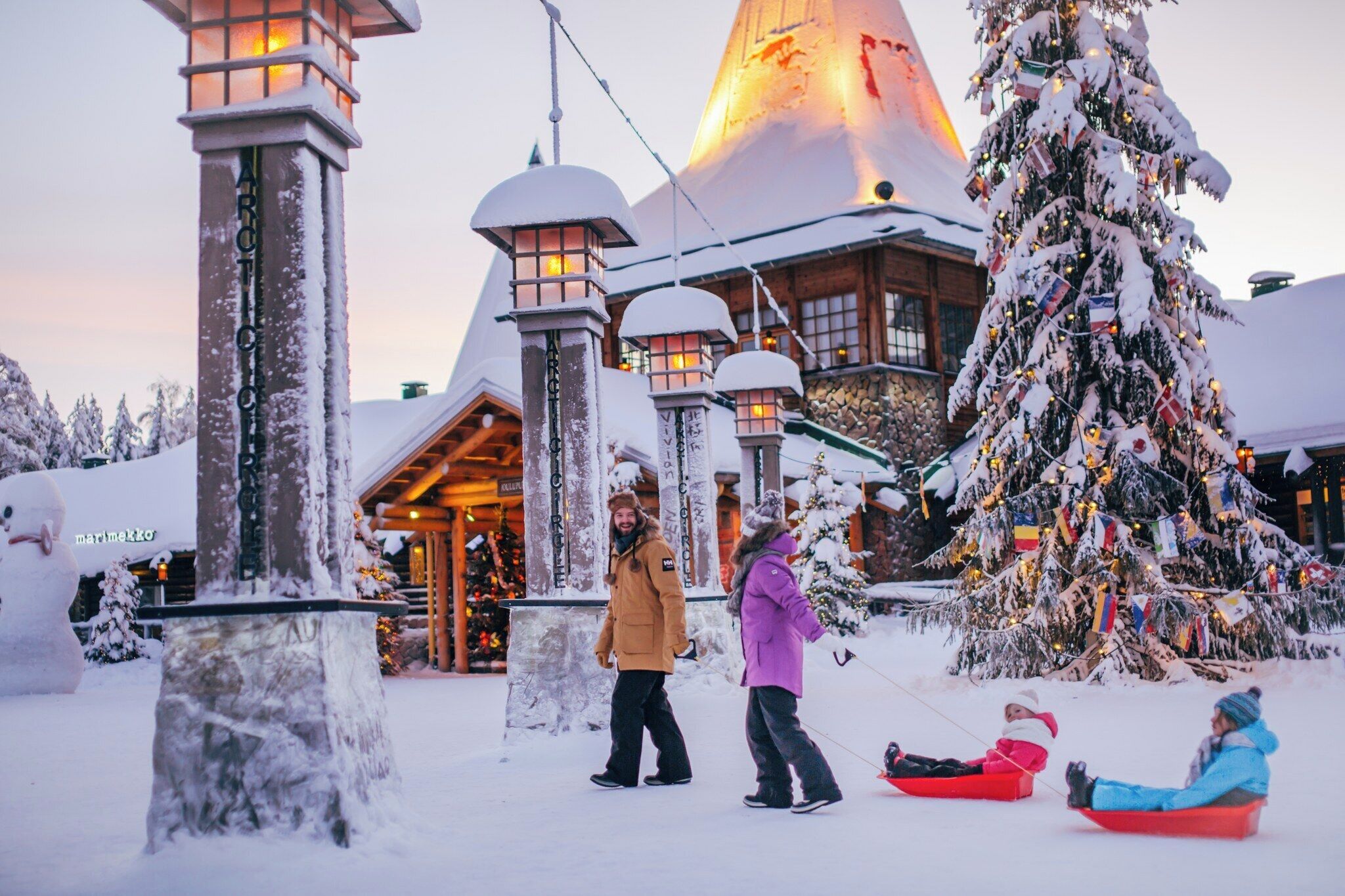 A snow-covered building with a large Christmas tree, a snowman, and people sledding.