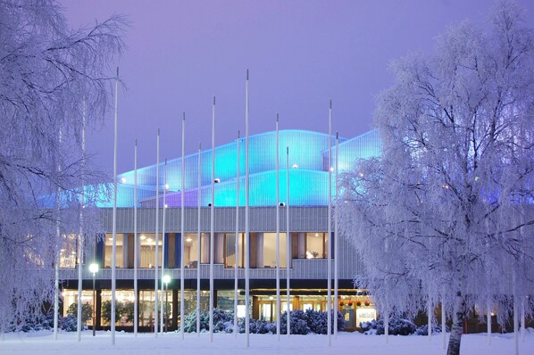 Un edificio moderno con fachada de vidrio y varios pisos, rodeado de árboles cubiertos de nieve.