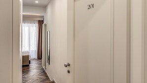 A hotel hallway with a door labeled "201", a bed in the background, and a herringbone-patterned floor. - EFFE LUXURY ROOMS (Rome)