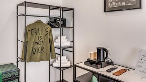A hotel room with a metal shelving unit holding a green shirt with text, a coffee machine, a remote control, and a welcome sign. - EFFE LUXURY ROOMS (Rome)
