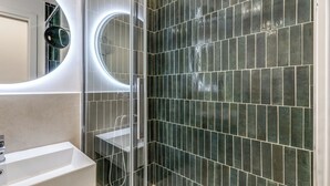 A modern bathroom with a glass-enclosed shower, a white sink, and a mirror with a circular frame. - EFFE LUXURY ROOMS (Rome)